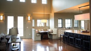 A spacious living area with a high ceiling, wooden beams, a central seating area with a table, and a kitchen with a large island and bar stools. - WATER FRONT - PRIVATE POOL AND DOCK W/BUOY (Manson)