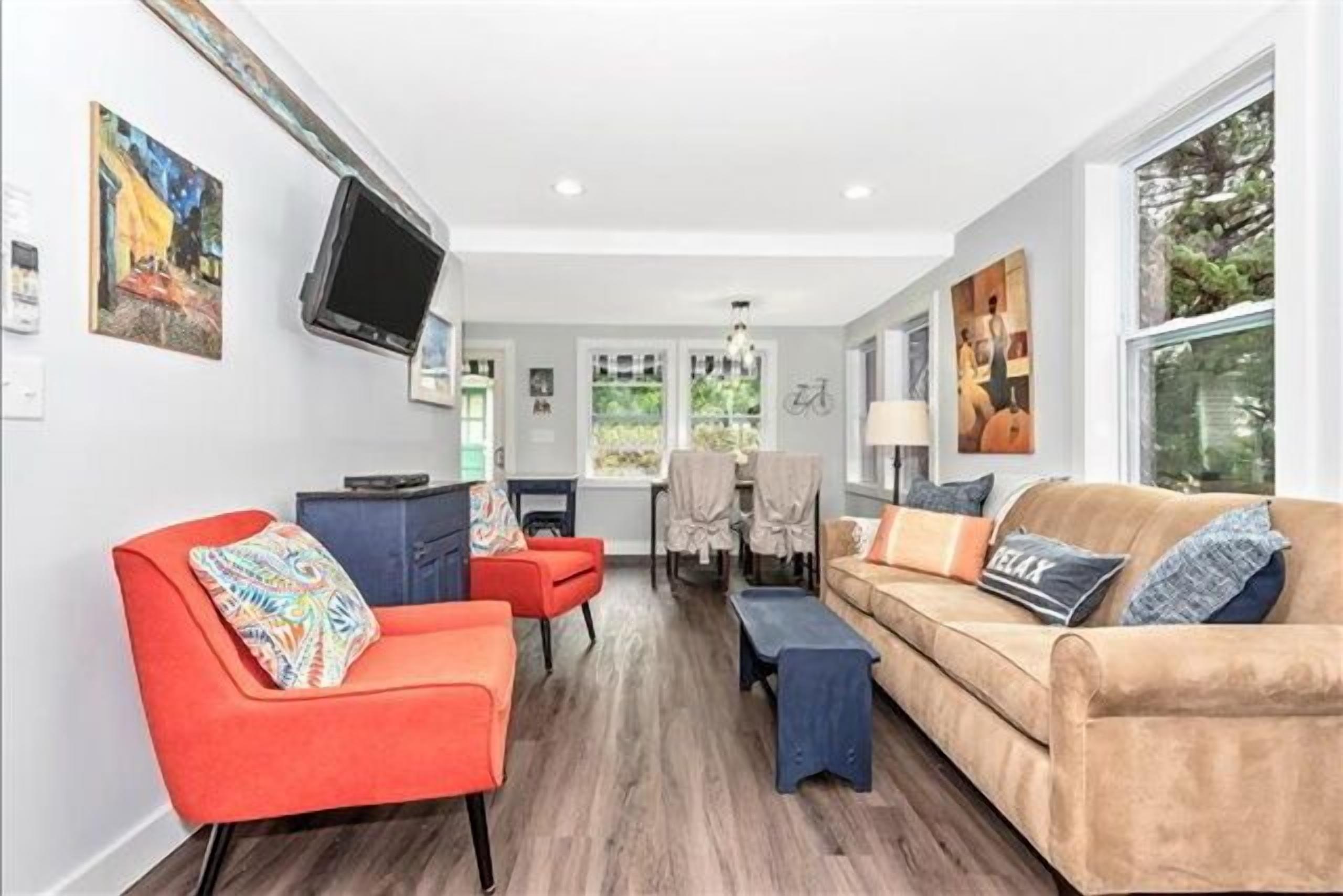 A modern living room with a sofa, armchairs, and a coffee table. There is a TV mounted on the wall and a dining area in the background.