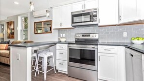 Uma cozinha moderna com armários brancos, eletrodomésticos de aço inoxidável e um espaço bar com banquetas.