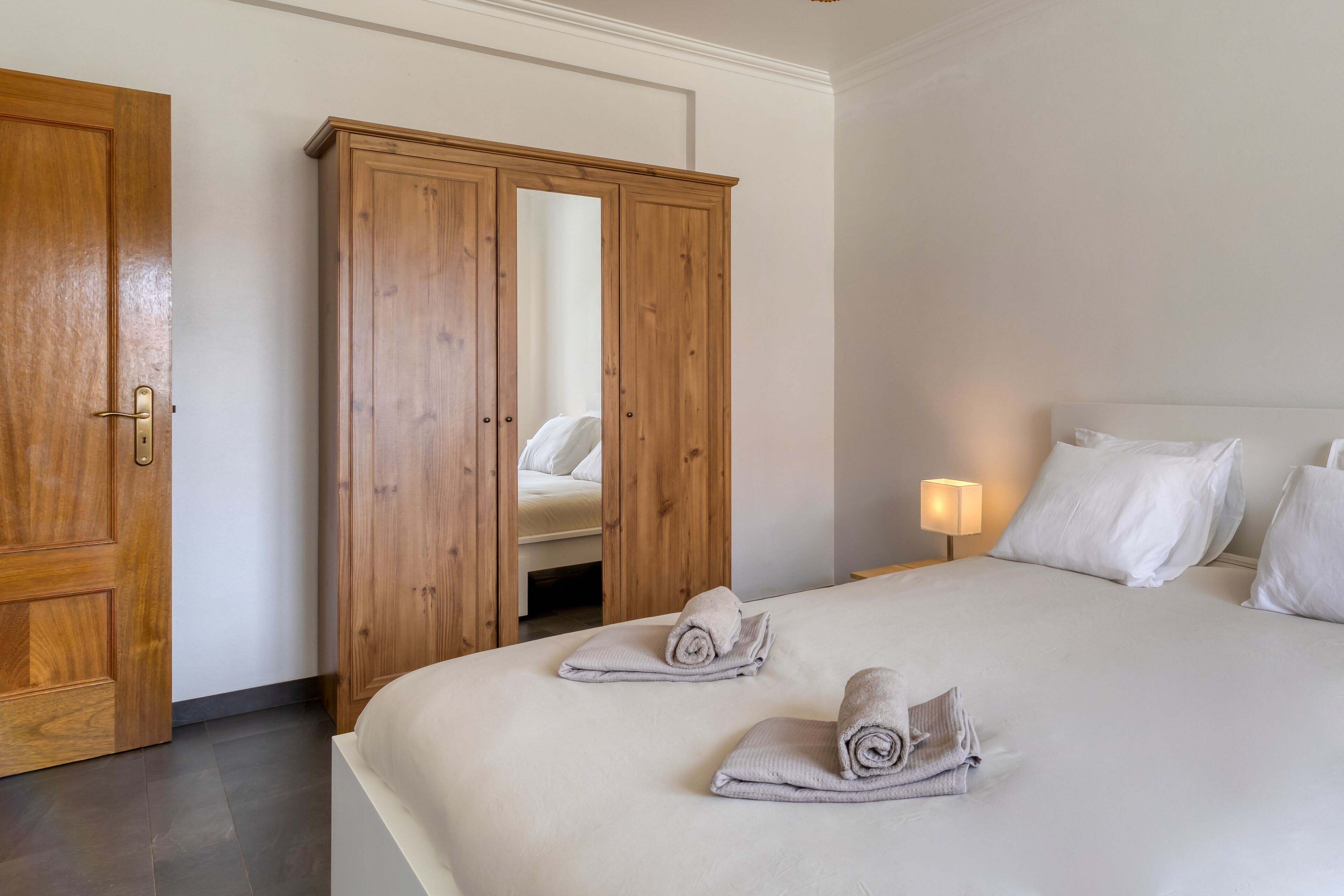 Een hotelkamer met een groot bed, een houten garderobe en een bedlampje.