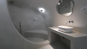 A modern bathroom with a freestanding bathtub, a round mirror, and a white sink. - Fira Getaway (Santorini)