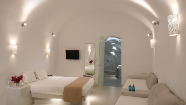 A modern, minimalist bedroom with a large bed, a sofa, and a small table. - Fira Getaway (Santorini)