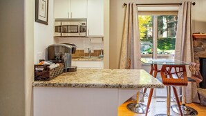 A kitchen with white cabinets, a microwave, a toaster, and a glass table with chairs. - Elkhorn Condo Walk to Dollar! (Sun Valley)