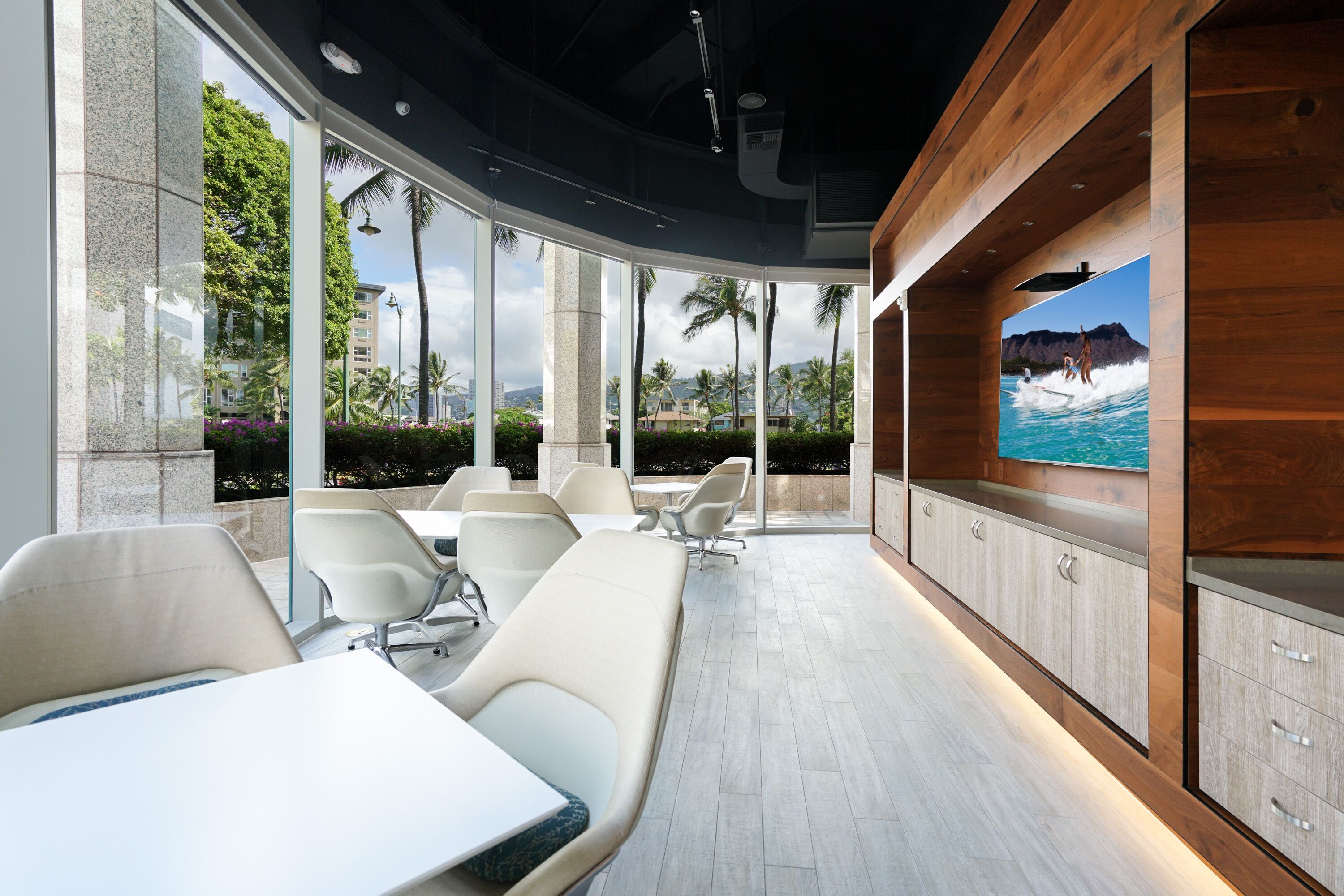 A modern lounge area with seating, a large TV screen, and a view of palm trees and buildings.