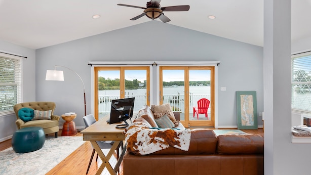 A modern living room with a brown leather sofa, a wooden dining table, and a large window overlooking a body of water.