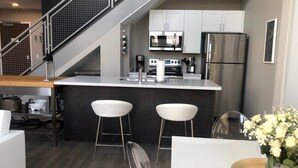 Cozinha moderna com armários brancos, eletrodomésticos de aço inoxidável e uma ilha central com banquetas.