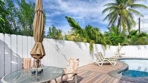 Una terraza de madera con una mesa de vidrio, sillones de descanso y una piscina.