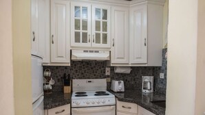 A kitchen with white cabinets, a stove, a toaster, and a coffee maker. - Sandcastles Bed & Breakfast Hotel (Ocho Rios)