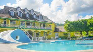 A swimming pool with a blue slide, surrounded by a yellow building with multiple windows and balconies. - Sandcastles Bed & Breakfast Hotel (Ocho Rios)