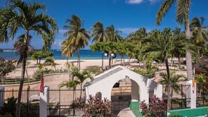 A beach view with palm trees, a white building with an archway, and a clear blue sky. - Sandcastles Bed & Breakfast Hotel (Ocho Rios)