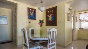 A dining area with a round table, four chairs, a vase with flowers, and two framed paintings on the wall. - Sandcastles Bed & Breakfast Hotel (Ocho Rios)
