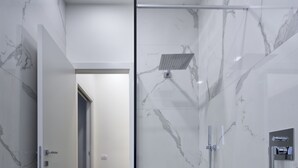 A modern bathroom with marble walls, a glass shower enclosure, and a wooden floor.