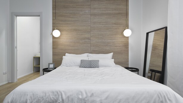 A modern bedroom with a large bed, two bedside tables, a wooden headboard, and a large mirror.