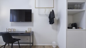 A modern room with a flat-screen TV mounted on the wall, a desk with a chair, and a white cabinet with shelves.