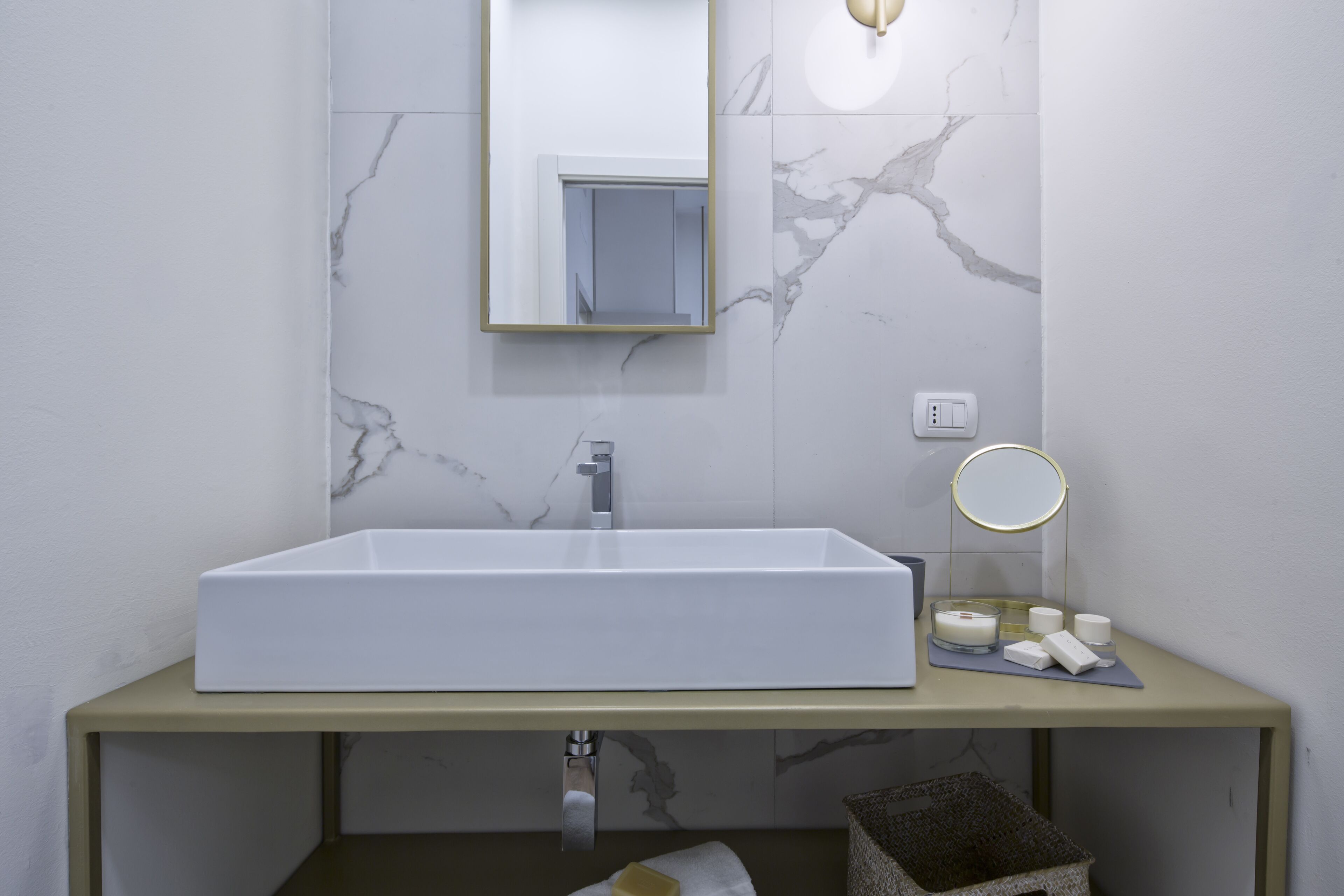 A bathroom with a white sink, a mirror, a round light, and toiletries on the counter.