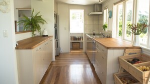 A modern kitchen with wooden countertops, a built-in oven, and a window providing natural light. - Oneroa Escape - Bell's Cottage (Waiheke Island)