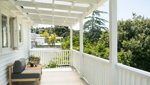 A covered porch with a white railing, a wooden bench, and a table with a plant. - Oneroa Escape - Bell's Cottage (Waiheke Island)