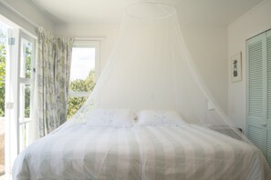 A bedroom with a bed, a window with curtains, and a door with shutters.