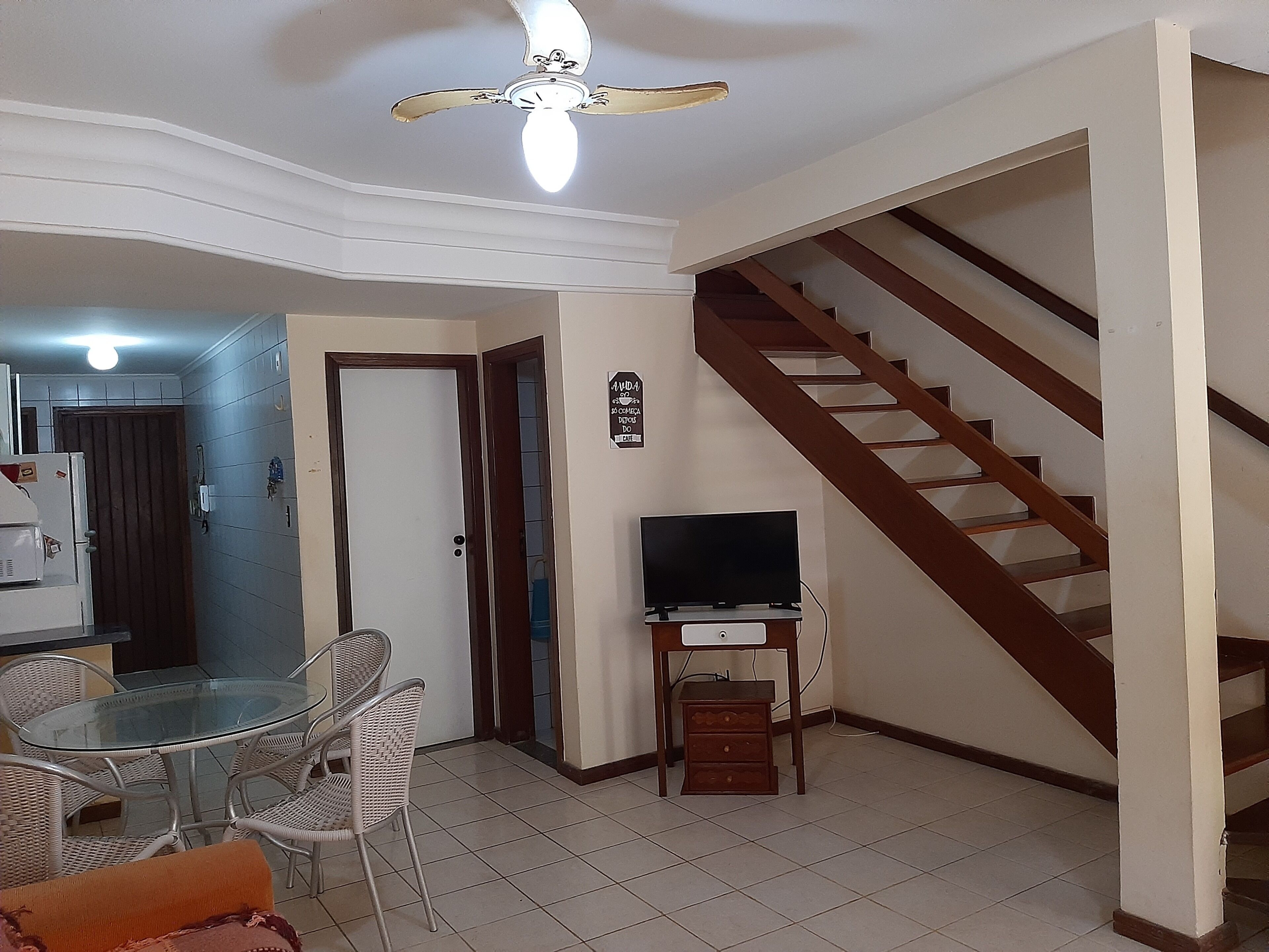 A living room with a dining area, a TV on a stand, a ceiling fan, and a staircase.