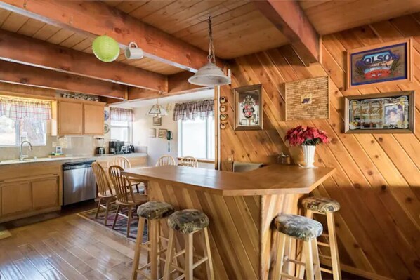 A wooden cabin interior with a kitchen, dining area, and bar. - Rustic Mountain Retreat. Trail access, fenced yard (Big Bear Lake)