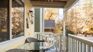 Une véranda aménagée avec des meubles en osier et une table en verre, donnant sur une cour avec des arbres et une maison.