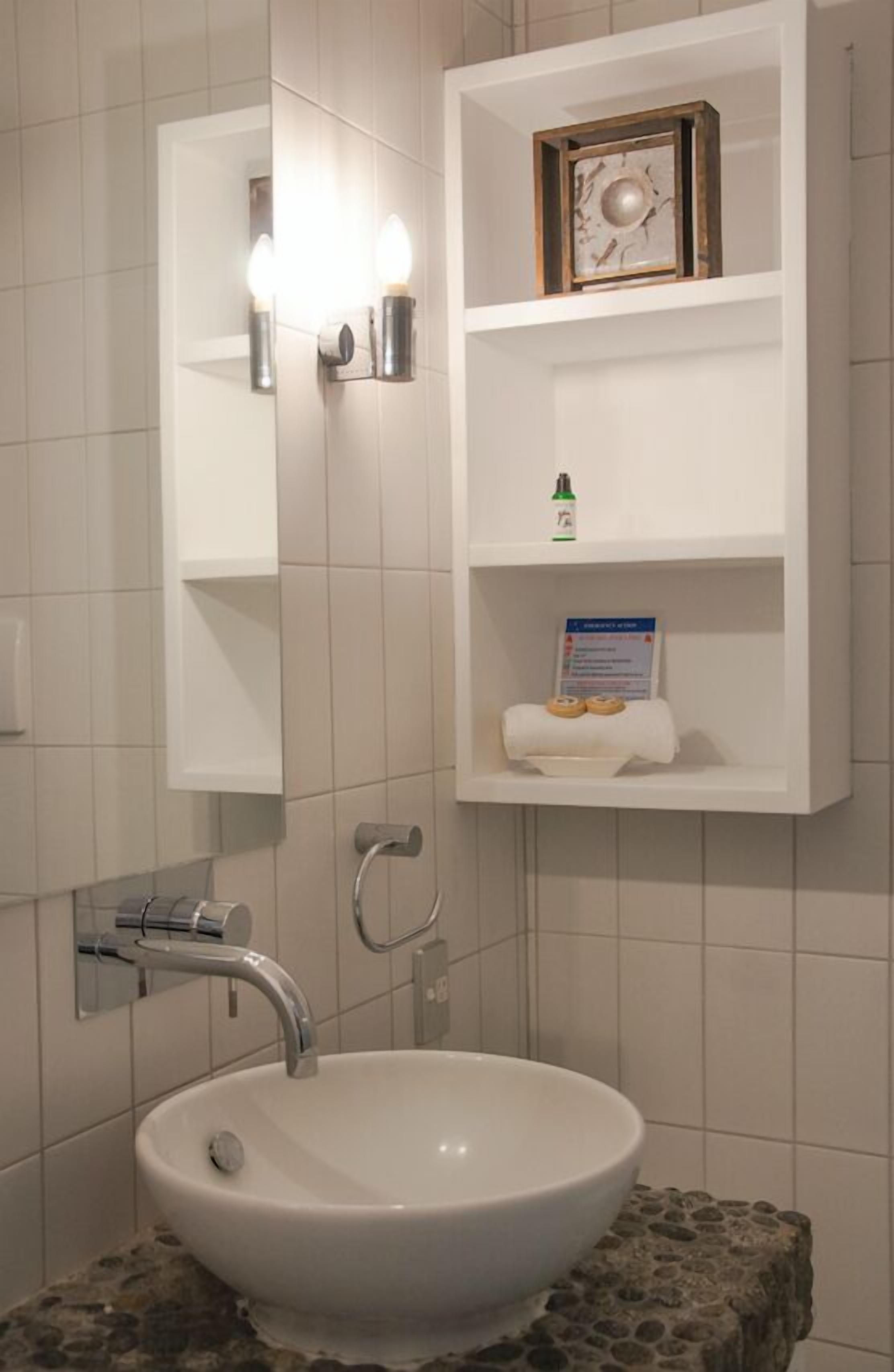 A bathroom with a white sink, a mirror, and a shelf with toiletries.