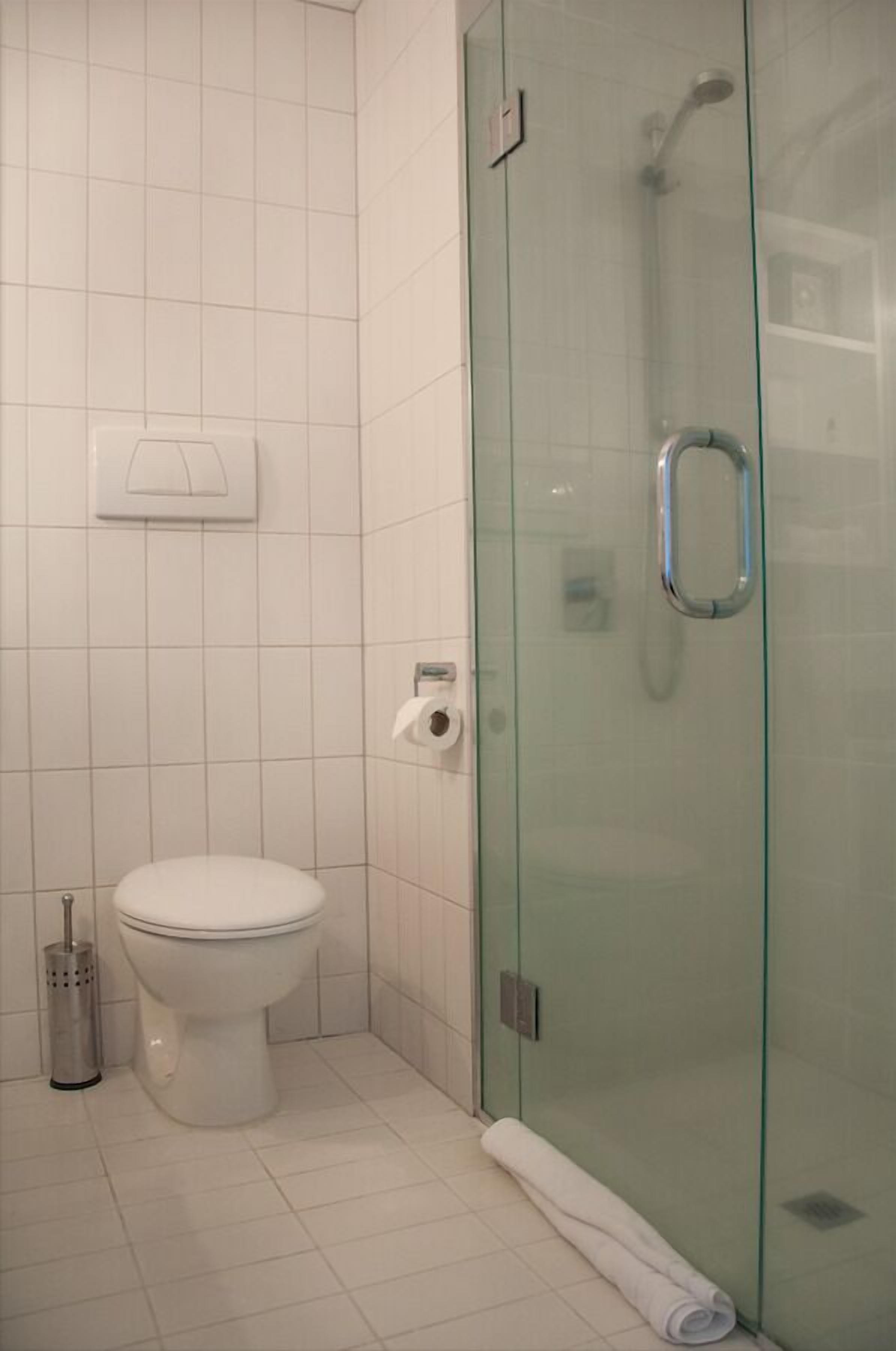 Ein Badezimmer mit Toilette, einer Duschkabine aus Glas und einem Handtuch auf dem Boden.