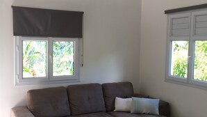A living room with a brown sectional sofa, a wooden coffee table with two candles, and a potted plant. - Kaymargo, Creole bungalow (Saint-Esprit)