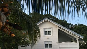 A white two-story house with a garage, surrounded by lush greenery and palm trees. - Kaymargo, Creole bungalow (Saint-Esprit)