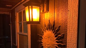 Pared externa de madeira com decoração em forma de sol e janela com luminária.