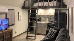 Um espaço compacto com quarto no mezanino, cozinha americana e área de estar com televisão.