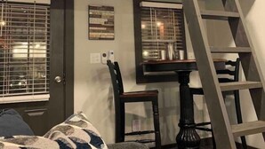 Quarto em estilo loft com escada de madeira, mesa de jantar e uma cadeira.