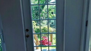A white door with a grid pattern, leading to an outdoor area with a wooden deck and greenery. - Panoramic view, large deck, ground floor apartment, walk to subway and beach (Boston)