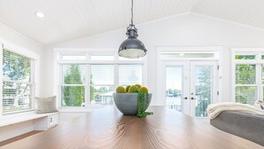Un vaste espace dédié à la salle à manger, avec une grande table en bois, un saladier de pommes vertes et un luminaire suspendu.