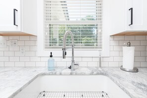 A modern kitchen with a white tiled backsplash, a stainless steel sink, and a window with blinds.