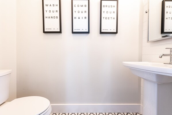 A bathroom with a toilet, sink, and three framed signs on the wall with hygiene instructions.