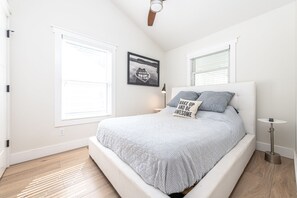 A bedroom with a bed, two windows, a ceiling fan, and a bedside table.