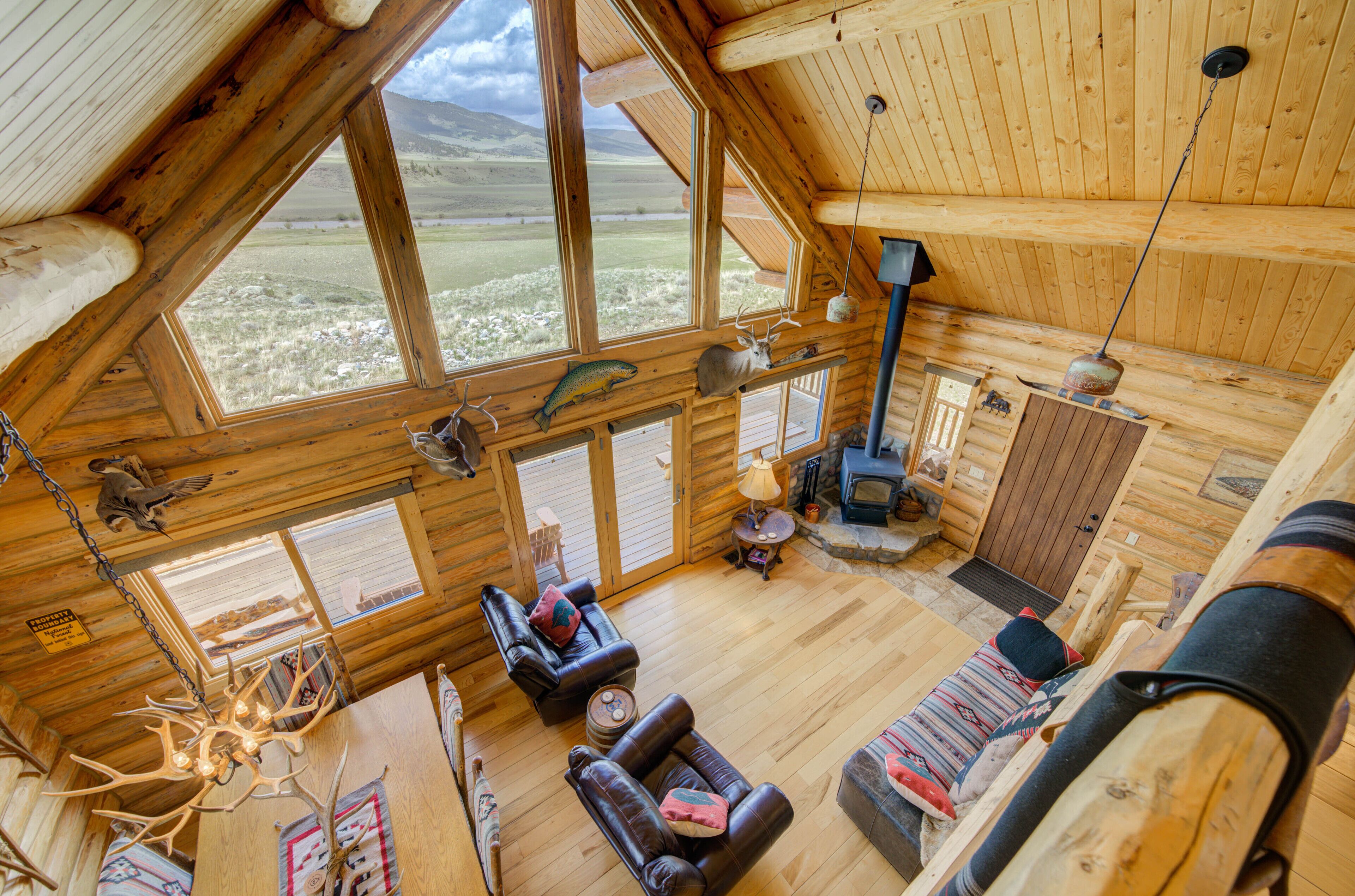 A log cabin interior with a large window, wooden furniture, a fireplace, and a hanging light fixture. - True Montana Log Cabin, Yellowstone Park, Ennis, Madison River Fishing,  4+2.5 (Cameron)