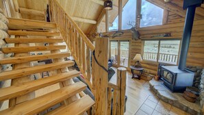 A wooden staircase leading to a deck with a stone fireplace and a large window overlooking a landscape. - True Montana Log Cabin, Yellowstone Park, Ennis, Madison River Fishing,  4+2.5 (Cameron)