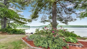 A landscaped garden with a tree, flower bed, and a view of a lake. - Private Beach! Kayak, Swim, Fish! Hot Tub, Sauna & Boat Dock. Year-Round Fun! (Harrison)
