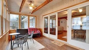 A cozy interior with a wooden ceiling, large windows, a sofa, a dining table, and a ceiling fan. - Private Beach! Kayak, Swim, Fish! Hot Tub, Sauna & Boat Dock. Year-Round Fun! (Harrison)