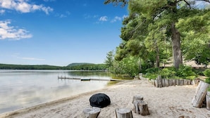 A beach with a wooden dock extending into calm water, surrounded by trees and a sandy shore. - Private Beach! Kayak, Swim, Fish! Hot Tub, Sauna & Boat Dock. Year-Round Fun! (Harrison)
