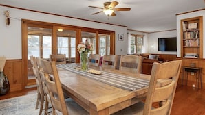A dining area with a wooden table, chairs, a vase with flowers, and a ceiling fan. - Private Beach! Kayak, Swim, Fish! Hot Tub, Sauna & Boat Dock. Year-Round Fun! (Harrison)