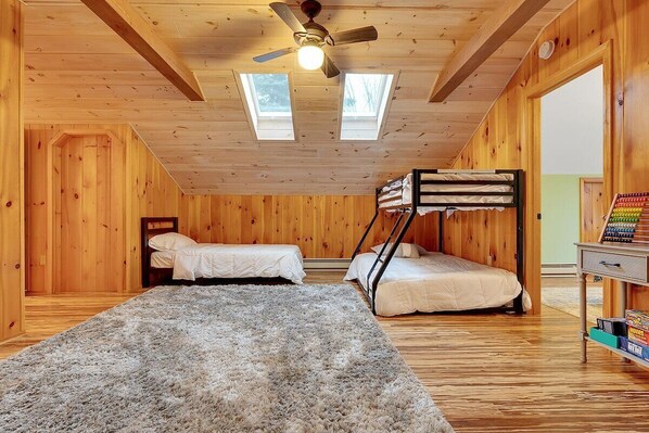 Een kamer met twee stapelbedden, een plafondventilator, dakramen en een boekenplank.