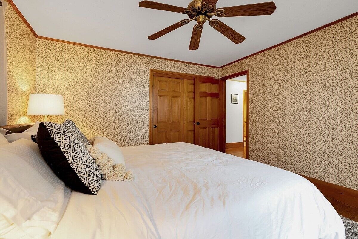 A bedroom with a bed, a ceiling fan, a wooden door, and a patterned wall.