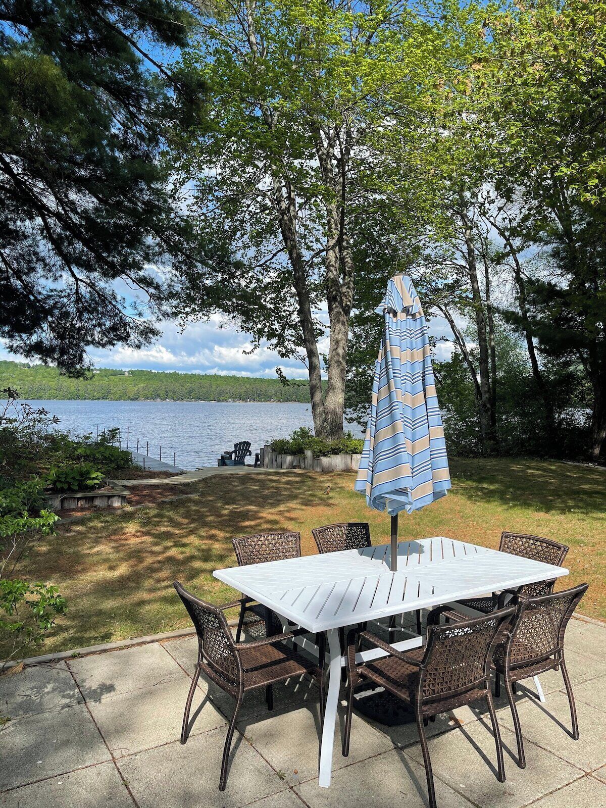 Une terrasse avec une table et des chaises, un parasol et une vue sur un lac.