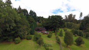 A large, open grassy area with a prominent red building in the center, surrounded by dense trees and well-maintained gardens. - Rent house villarrica-pucon (eclipse 2020) (Villarrica)