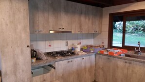 A kitchen with wooden cabinets, a gas stove, a sink, and a window with a view of greenery. - Rent house villarrica-pucon (eclipse 2020) (Villarrica)