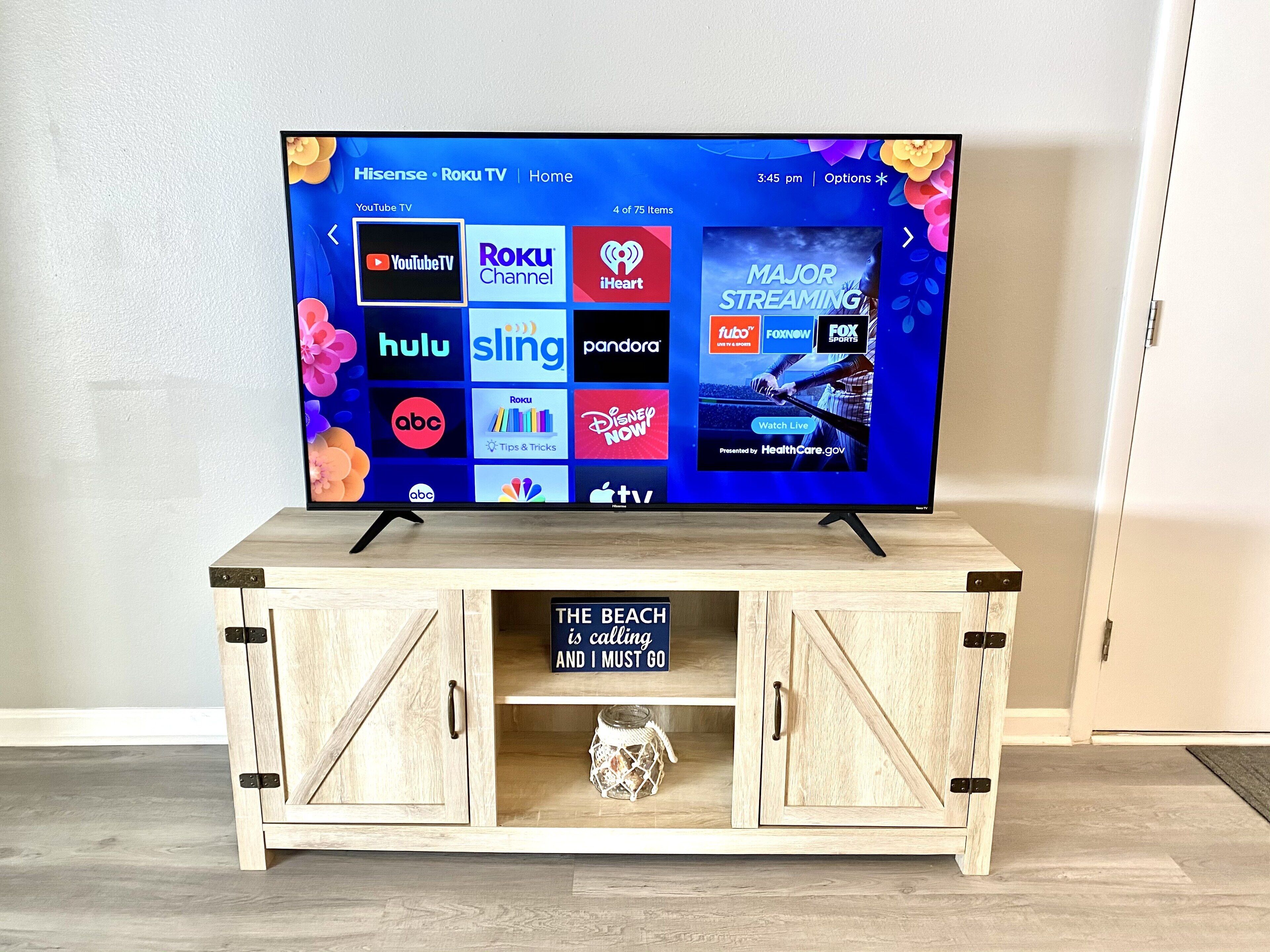 Un televisor sobre un mueble bajo de madera con un cartel que dice 'La playa me llama y debo ir'.