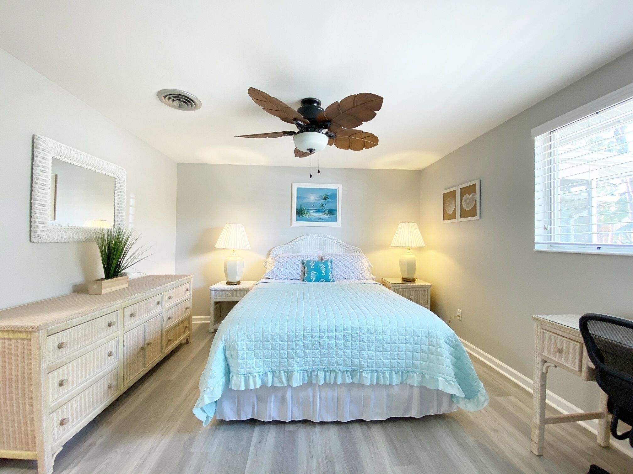 Une chambre à coucher comprenant un lit, deux tables de chevet avec des lampes, un ventilateur de plafond, une commode, une chaise et une fenêtre.